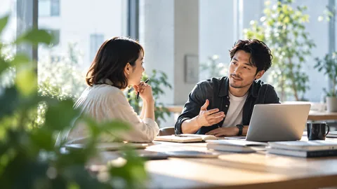 明るい室内で、ノートパソコンを前に二人が話している